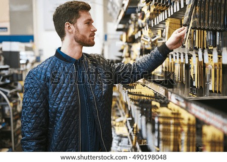 Bearded young man in a hardware store standing reading the information on a product hanging on the rack, side view close up