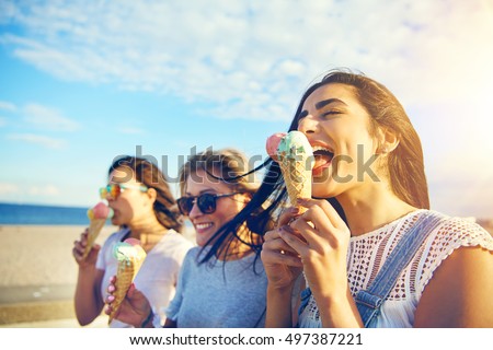Tres jovencitas comiendo helados en la costa mientras caminan por un paseo marítimo en un caluroso día de verano durante sus vacaciones