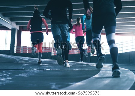 Back view of sportsmen running in a group outdoors over urban background. Copyspace.