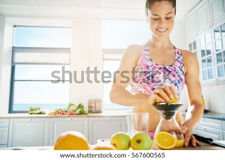 Happy sporty woman standing in sunlight in the kitchen making juice. Horizontal indoors shot