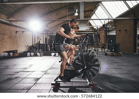 Side view of young people in sportswear sitting and riding on cycling machines in spacious modern gym. 