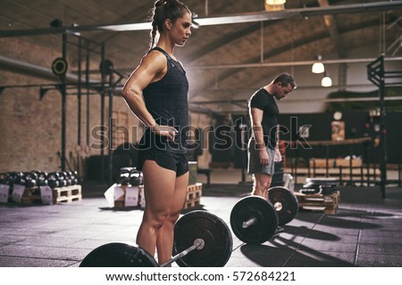Sporty muscular people standing at barbells in gym. Horizontal indoors shot