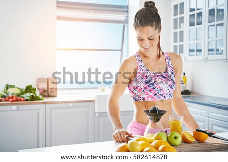 Happy young woman with muscular body standing in the kitchen while making fresh. Horizontal indoors shot