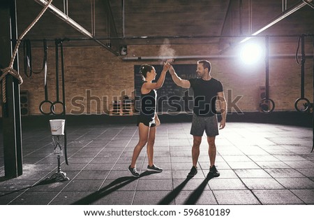 Young muscular sportsman and sportswoman exchanging high five in gym. 