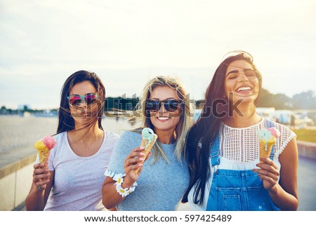 Tres alegres novias jóvenes en un paseo junto a una hilera sonriendo alegremente mientras disfrutan tomando helados en las vacaciones de verano