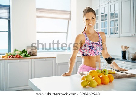 Sporty woman standing near fruits and juicer at the kitchen. Horizontal indoors shot