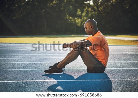 Focused young African male athlete in sportswear sitting alone on a running track mentally preparing for a race