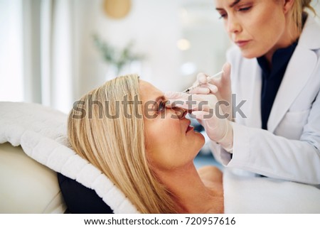 Young female doctor performing a botox injection to the forehead of a mature woman lying on a table in a beauty clinic