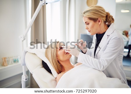 Young female doctor performing injections on the forehead of a mature woman lying on a table in a beauty clinic