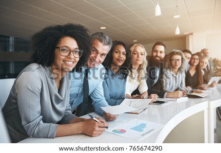 Portrait of a smiling group of diverse corporate colleagues standing in a row together at a table in a bright modern office