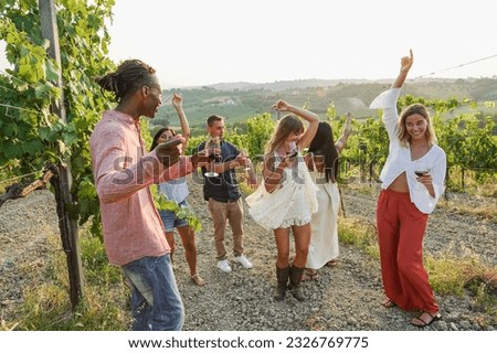 Amigos multirraciales bailando en la fiesta de verano dentro de los viñedos - Gente feliz divirtiéndose juntos bebiendo vino tinto en el complejo rural - Concepto de viaje, celebración y evento de cata - Enfoque en caras