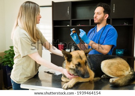 Handsome veterinarian giving a bottle of medicine to a caucasian woman for her sick german shepherd. Male vet holding prescription pills for the injury and pain of a dog