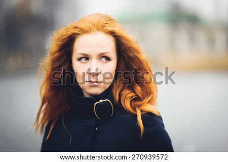 Beautiful red-haired girl posing in autumn park and smiling