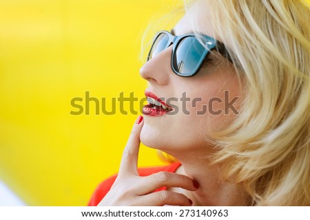 bright portrait of a beautiful young blonde girl on a yellow background with red lips and nogtyamy and smile and sunglasses