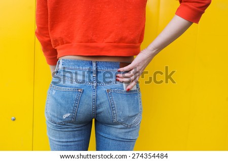 Booty young slim girl in jeans and a red blouse on a yellow background, and the phone in your pocket