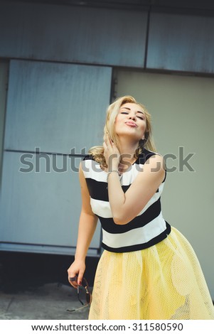 close-up portrait of a beautiful charming girl hipster blonde in a striped blouse and yellow skirt laughing and posing with full lips