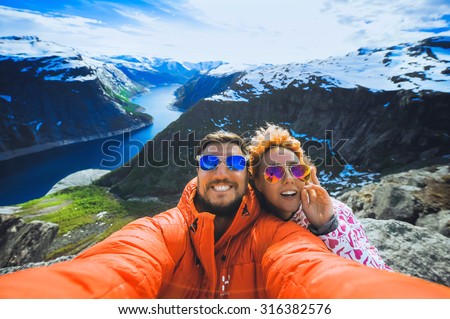 close-up portrait, selfi, happy couple  hipster young girl with red hair and a man with a beard in sunglasses in the mountains of Norway, in the language of a troll in a bright sportswear at sunset