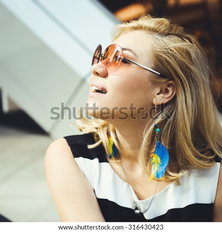 close-up portrait of a beautiful charming girl hipster in sunglasses blonde with full lips in a striped blouse laughing and posing