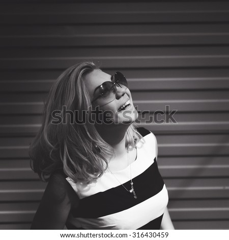 close-up portrait of a beautiful charming girl hipster in sunglasses blonde with full lips in a striped blouse laughing and posing