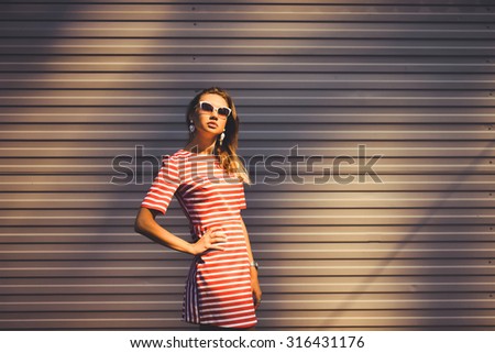 close-up portrait of a beautiful charming girl hipster in sunglasses blonde with full lips in a striped dress laughing and posing