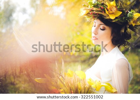 close-up portrait of a beautiful young sexy girl brunette bride with flowers in her hair look attractive in a white dress on a background of autumn forest and leaves posing and smiling
