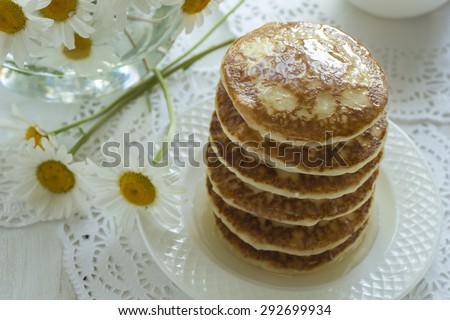 A stack of pancakes on a white table from boards and chamomile flowers