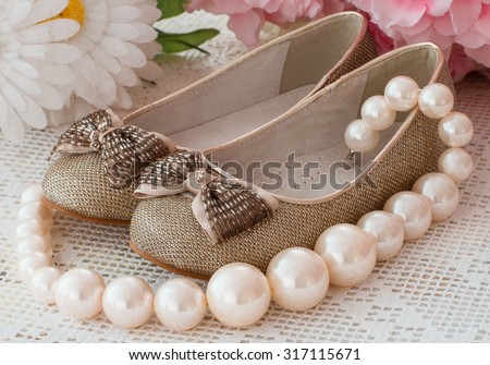 shoes of the Cinderella stand on an openwork cloth, a pearl beads, on a background flowers lies nearby