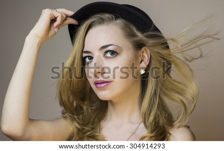 Beautiful girl in a black hat. Blonde with developing hair. Girl with big blue eyes.
