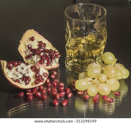 Still life with grapes and pomegranate. A glass of grape juice is on the table, a bunch of grapes and pomegranate are near.