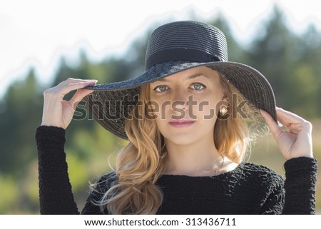 Girl in a black hat walks in the woods. Blonde in a black hat. A girl with long blond hair in a black wide-brimmed hat.