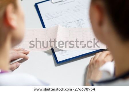 Two female doctors examining patient cardiogram chart. Professional conversation, council of cardiologists. Working conference. Medical concept