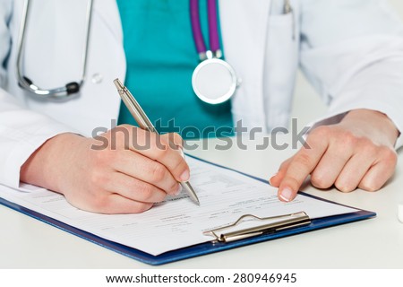 Female medicine doctors hands filling patient medical form. Physician working with paper in hospital office room. Therapeutist sitting at working table making some paperwork. Hands holding silver pen