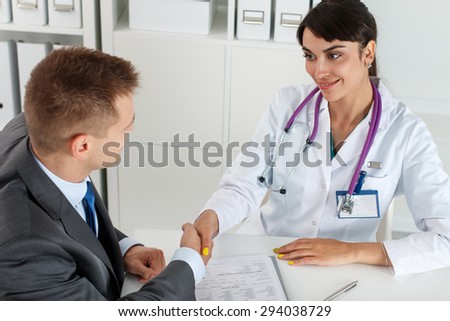 Beautiful smiling female medicine doctor shaking hands with male patient. Partnership, trust and medical ethics concept. Handshake with satisfied client. Thankful handclasp for excellent treatment