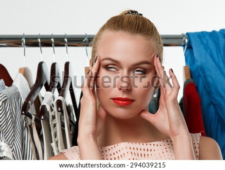 Beautiful blonde woman suffering near wardrobe rack full of clothes choosing dress to wear. Nothing to wear, hard to decide or stylist concept