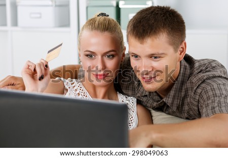 Family couple making shopping over internet looking in notebook and paying with credit card. Husband and wife buying new stuff in house. Shopping, consumerism, delivery and present concept