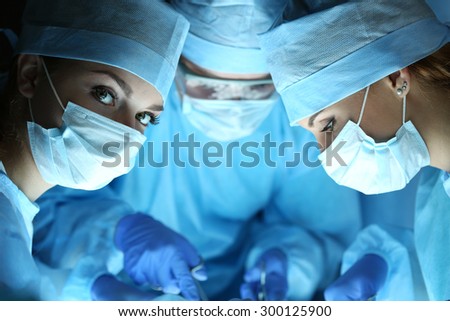Group of surgeons at work operating in surgical theatre. Resuscitation medicine team wearing protective masks holding steel medical tools saving patient. Surgery and emergency concept
