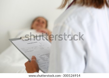 Female medicine doctor filling in patient medical history list during ward round. Medical care or insurance concept. Physician ready to examine patient and help. Patient sleeping