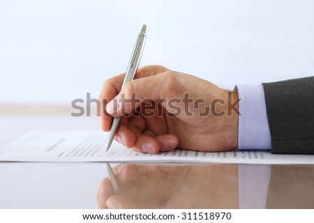 Hand of businessman in suit filling and signing with silver pen employment contract form lying on table with reflection closeup. Business success, agreement, paperwork or lawyer concept
