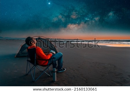 man sitting in a camping chair alone on the beach looking at the starry night next to a tent Foto stock © 