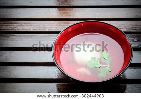 A bowl of clear chicken broth on a wood table top.