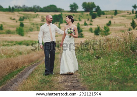 a happy just married couple is walking down a field path