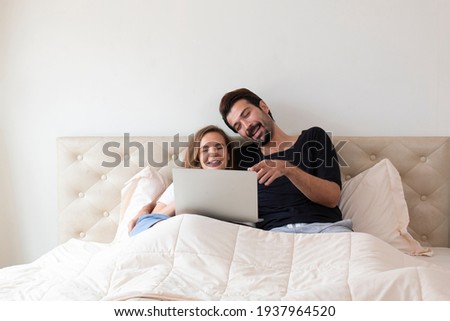 Happy Couple watching movie by laptop. Young couple watching a movie on bed at home in the afternoon. Man and woman watching movie from computer notebook on their bed.