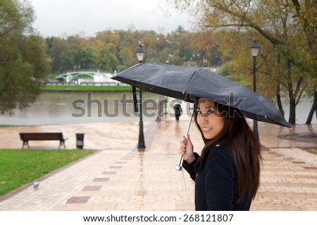 Beautiful girl walking in a park, looking back while holding umbrella