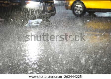 Heavy rain hitting a concrete sidewalk while cars drive by