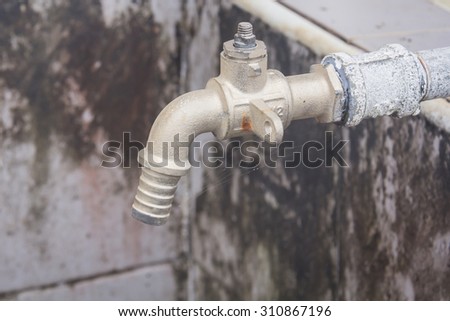 The picture of the old rusty water tap, crocked film. Under the tap is a plastic bucket with dirty water.