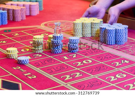 Casino American Roulette gambling table with a playing chips on the layout. Croupier is doing payout.