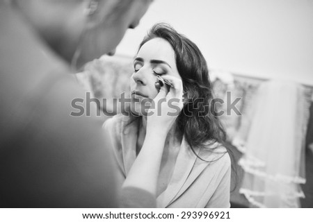 Young brunette bride applying wedding make-up by make-up artist
