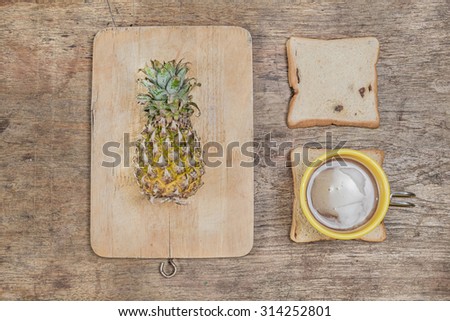 office wooden table with Chopping Board and pineapple cup of coffee and slice of bread, top view