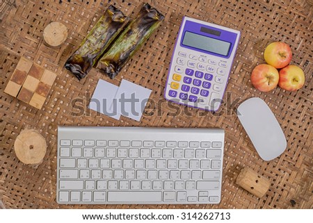 office wooden table with computer keyboard and computer mouse with calculator and paint brush with glasses, pencil, paper, and apple , top view