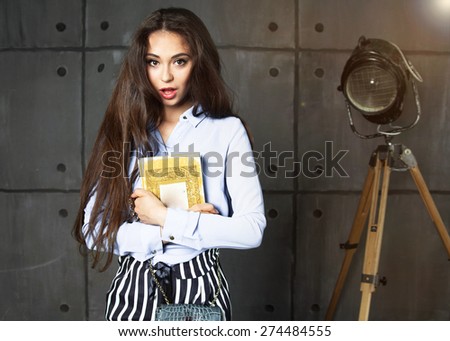 Young beautiful happy stylish hipster girl,reading book,surprised, fashion office style, teen, cool accessories, purse, amazed, vintage style, wall background, hair, wind,business style,suit